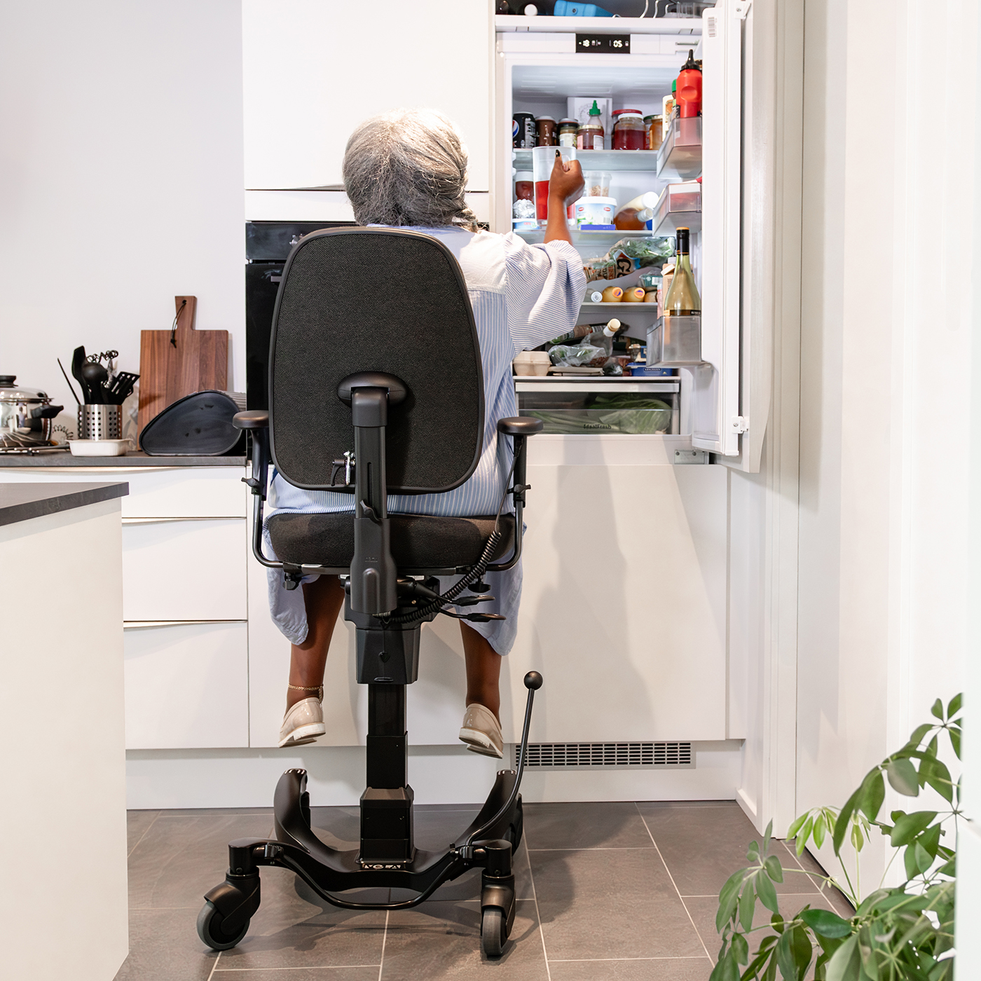 Ältere Frau nimmt etwas aus dem Kühlschrank in ihrer eigenen Wohnung für behinderte Menschen.