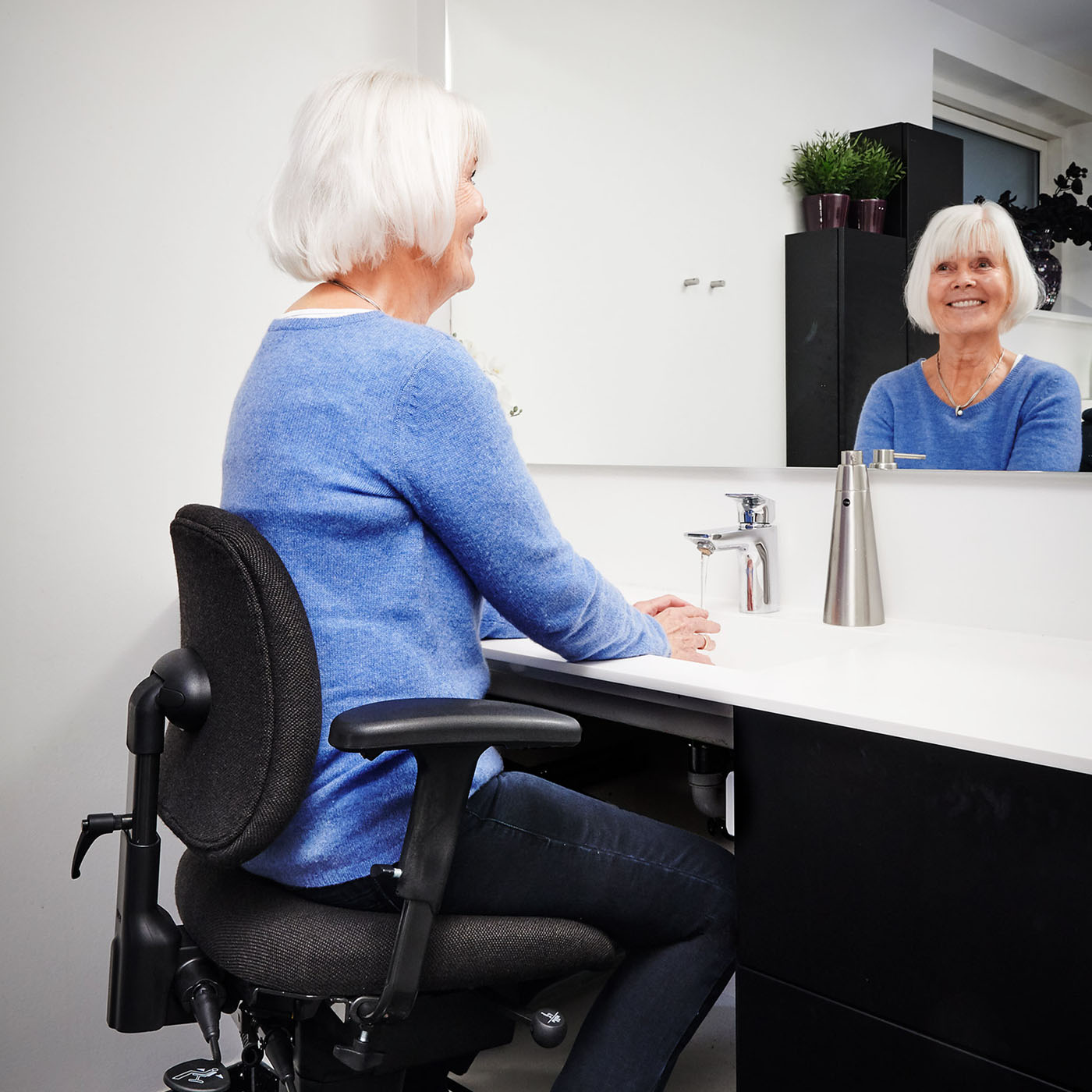 Ältere Frau benutzt den Trippelstuhl im Badezimmer beim Händewaschen