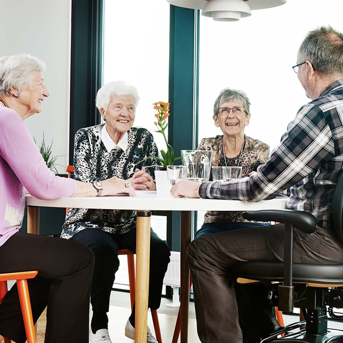 Vier Senioren sitzen um den Tisch, die eine Person sitzt im Seniorenstuhl.